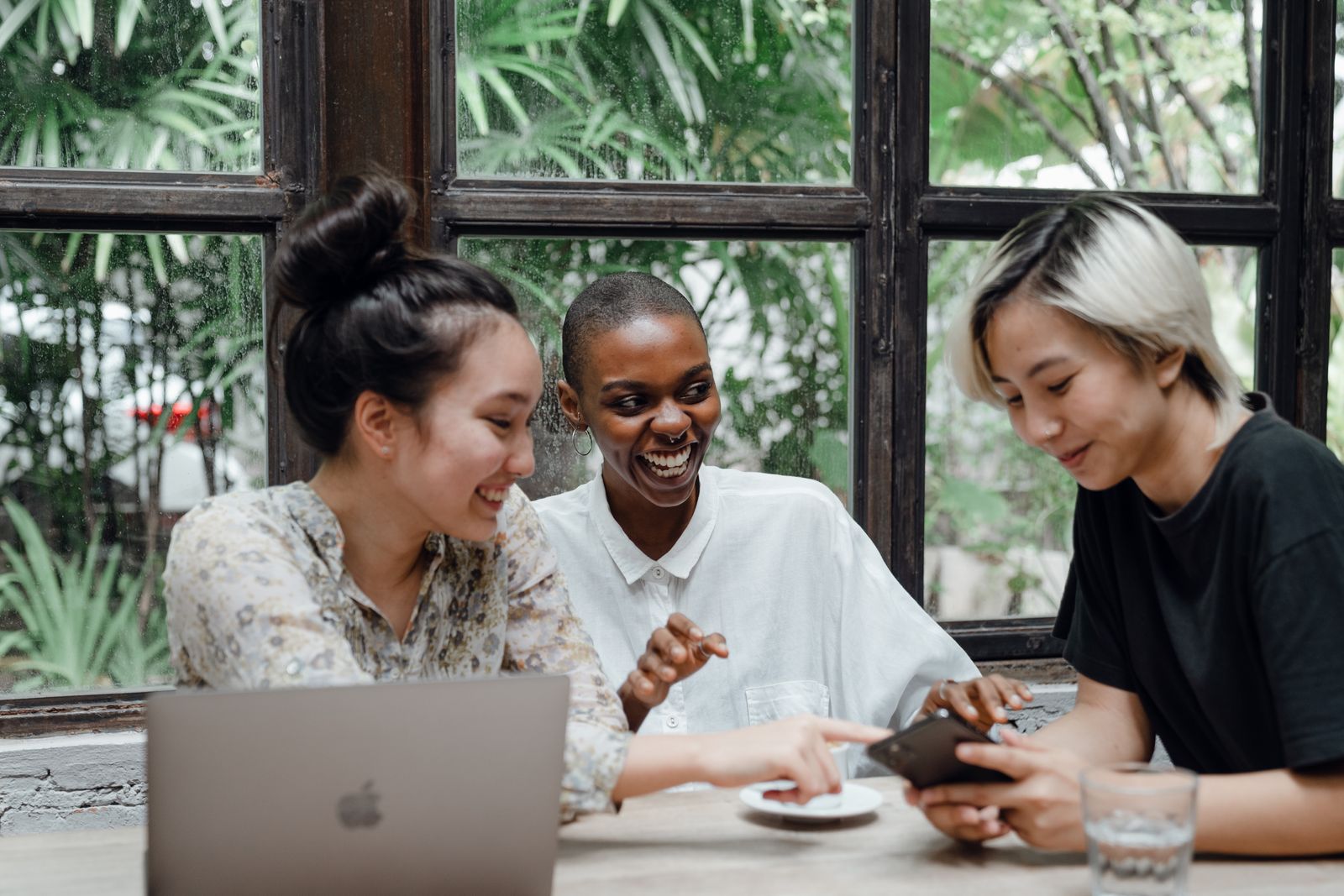 A group of friends smiling together while looking at a phone at a café table